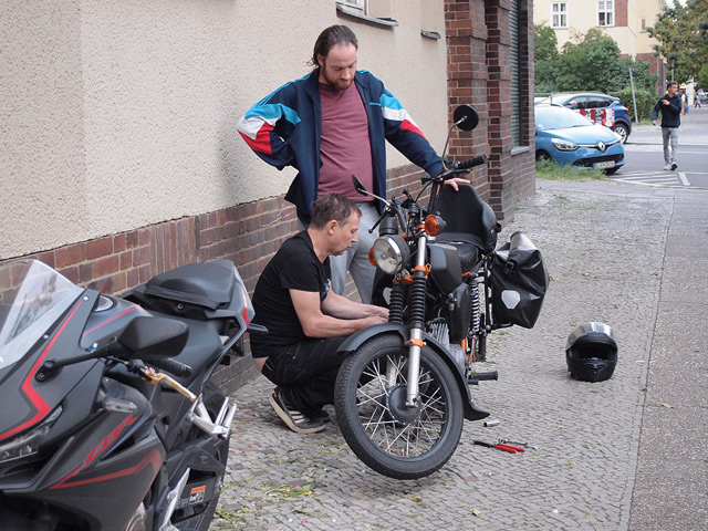 Two men repairing a motorcycle on the sidewalk.